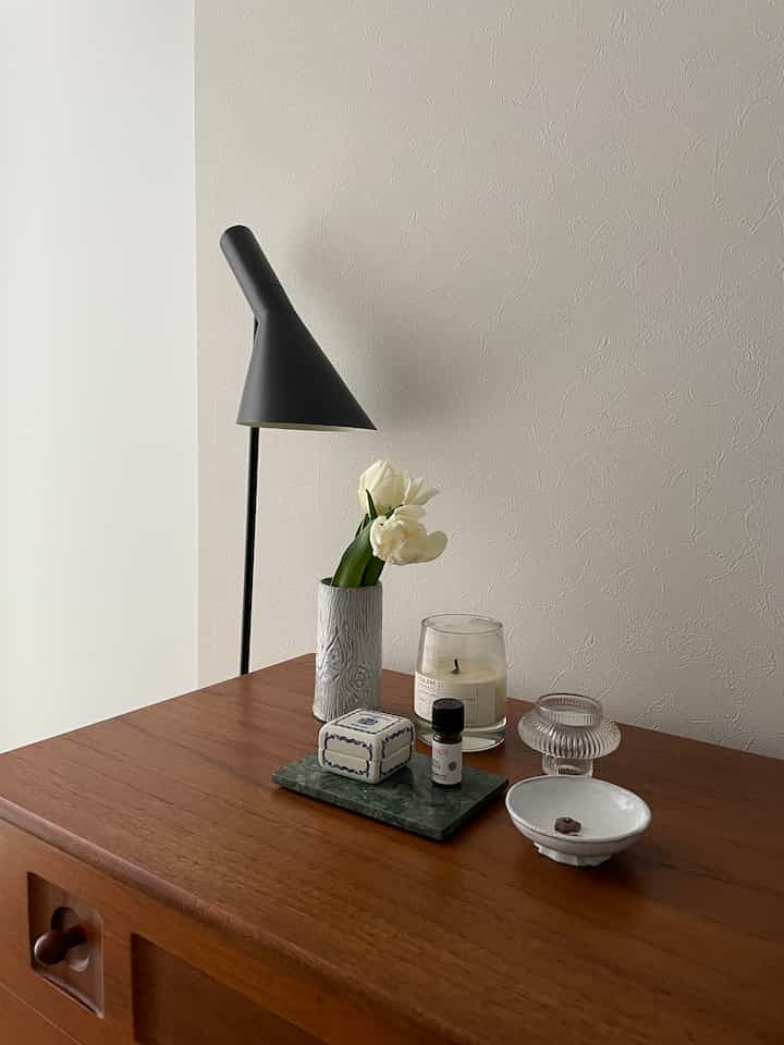 ブラウンの木製ドレッサーの上に白いチューリップとキャンドル、ディフューザーが置かれたナチュラルでミニマルなインテリア