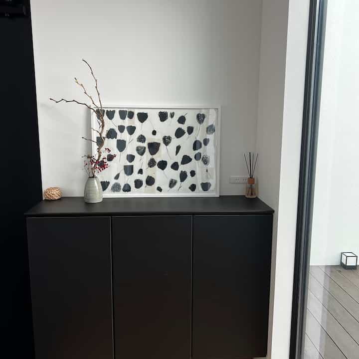 白い壁の玄関スペースに黒いシューズラックが配置され、ポスターとディフューザーが調和した落ち着いたインテリア