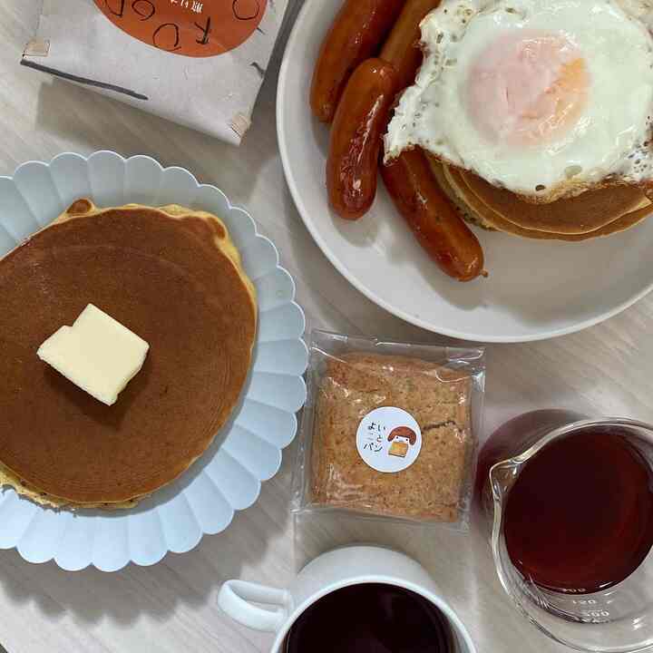 白を基調としたキッチンテーブルにパンケーキ、目玉焼き、ソーセージ、コーヒーが配置されたシンプルな朝食のインテリア