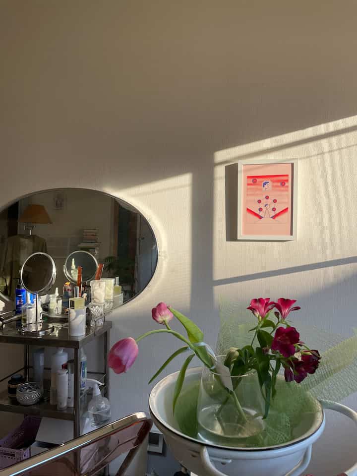 陽光が差し込む白い壁のリビングルームに花瓶、楕円形の鏡、額装されたウォールアートが配置された自然な雰囲気のインテリア