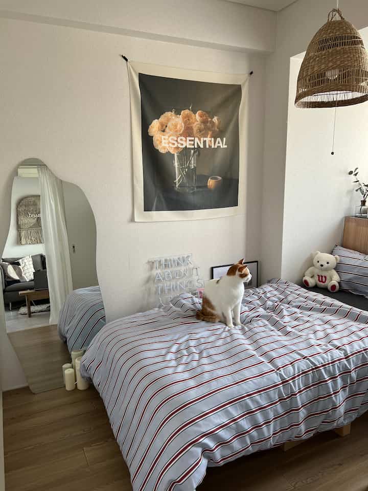 白とネイビーストライプの寝具がある寝室、ベッドの上に猫が座り、自然な雰囲気のあるインテリア