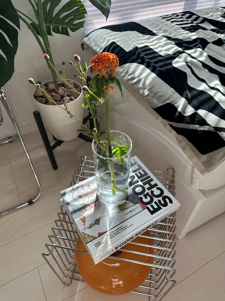 ナチュラルな色調のリビング、クローム製ワイヤーサイドテーブルに花瓶と本が置かれた落ち着いた空間