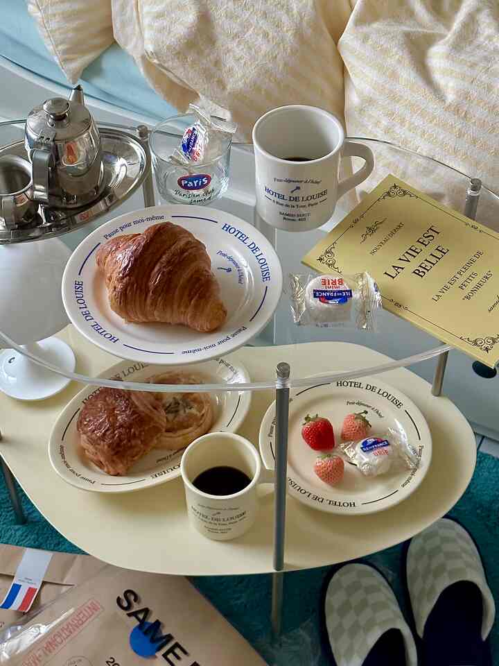 パステルトーンのベージュテーブルと青いクッションがあるおうちカフェ風リビング、クロワッサンとコーヒーが置かれたテーブル