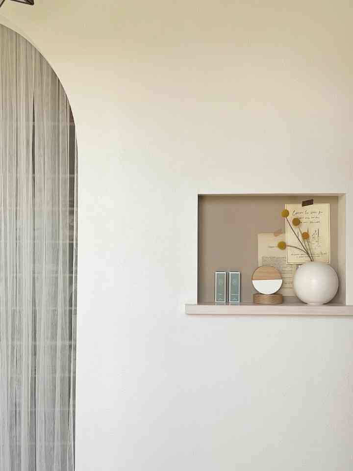 ナチュラルな色調の玄関、壁のニッチ棚に花瓶や装飾品が置かれ、薄手のカーテンが配された印象的な空間