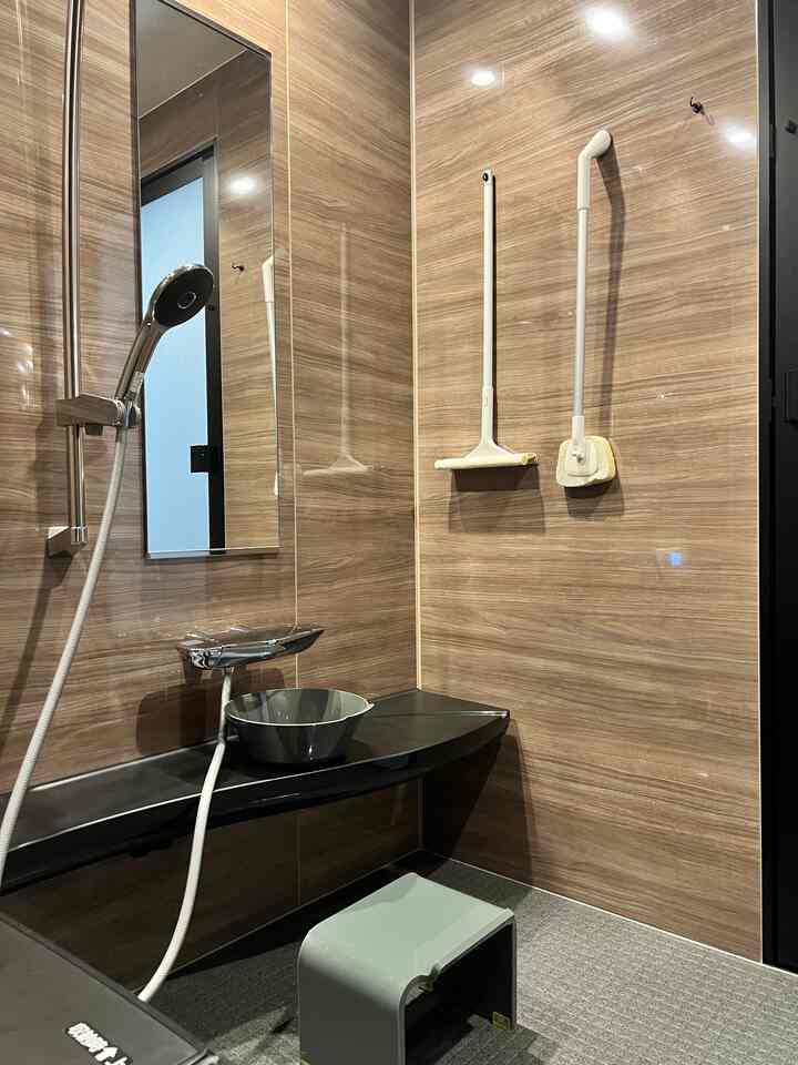 木目調の壁と黒い棚、グレーのスツールとステンレス製のボウルが配置されたシンプルなバスルーム