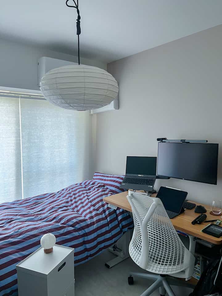 White and burgundy toned small bedroom featuring a dual-monitor desk setup with a Herman Miller chair for personal workspace