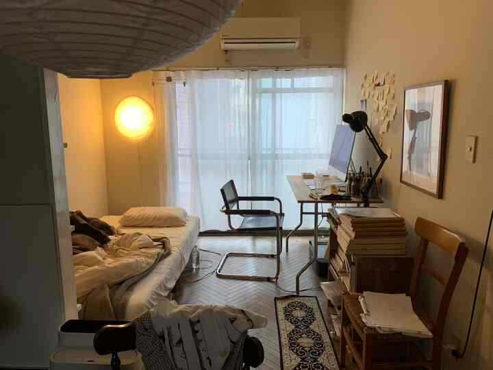 ナチュラルな木製の床とシングルベッド、デスクと椅子が配置された落ち着いた雰囲気の一人暮らしの狭い部屋