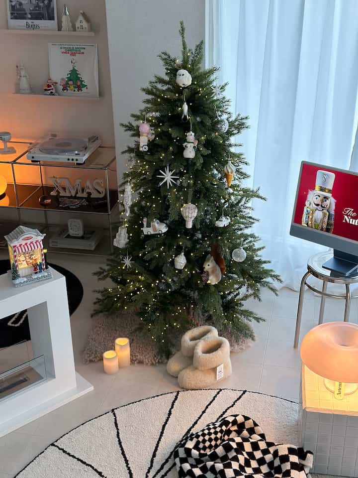 白い壁とカーテンのリビング、ナチュラルグリーンのクリスマスツリーとストリングライトが配置されたトレンディなインテリア