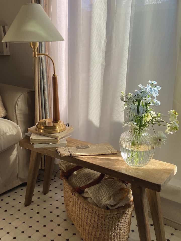 木目調のナチュラルなリビング、木製ベンチとフロアランプ、花瓶が温かみのある雰囲気を作り出す空間