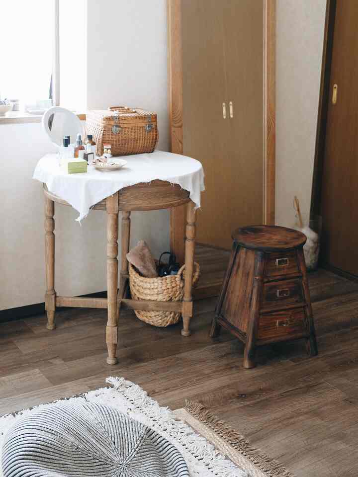 A cozy walk-in closet space with beige walls and wood tones featuring a round dresser table and wooden stool in a natural setting