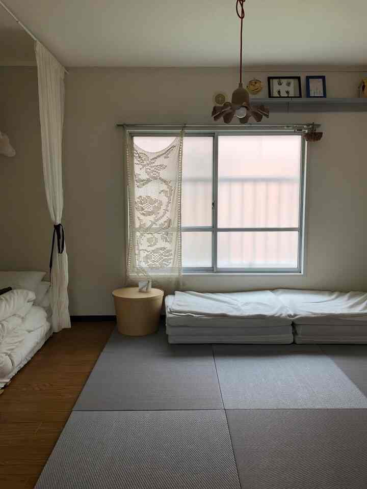 ベージュの色調のワンルーム寝室、窓際に畳風マットレスと枕が配置された自然な雰囲気のインテリア