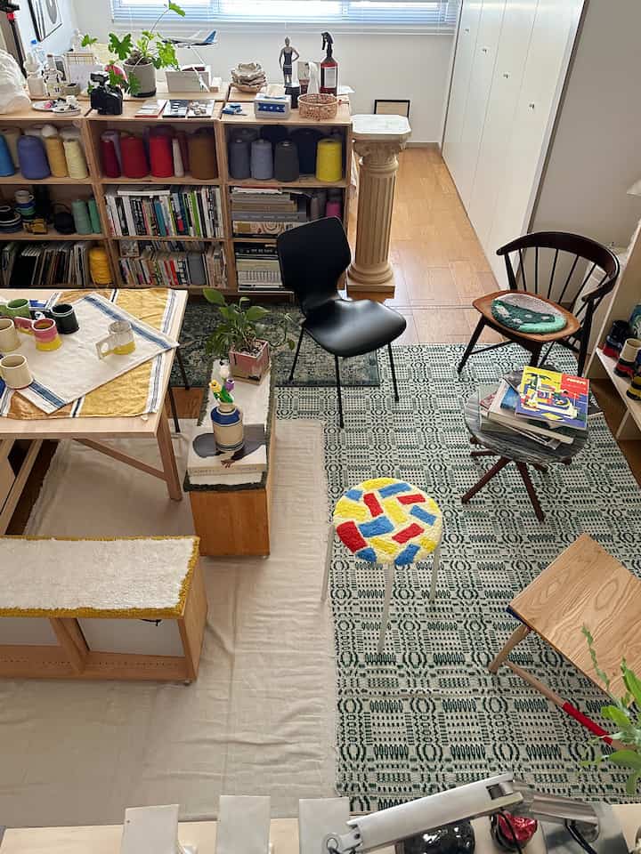 Natural wood tone flooring and bookshelf with rugs and various chairs arranged in a cozy living room space