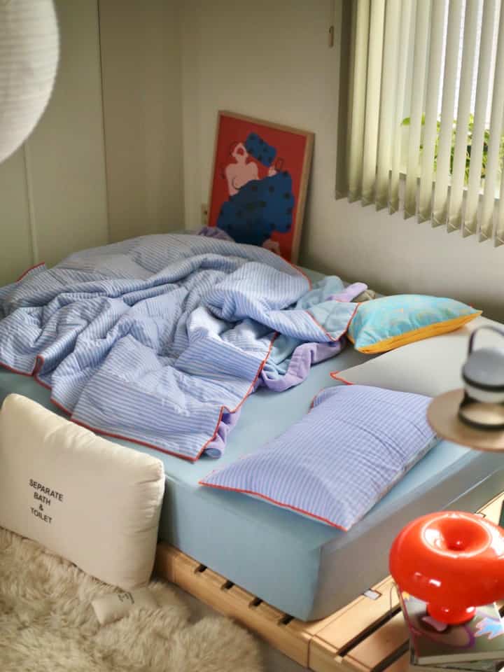 Cozy small bedroom with blue bedding and orange accents, featuring a retro-style table lamp and framed artwork