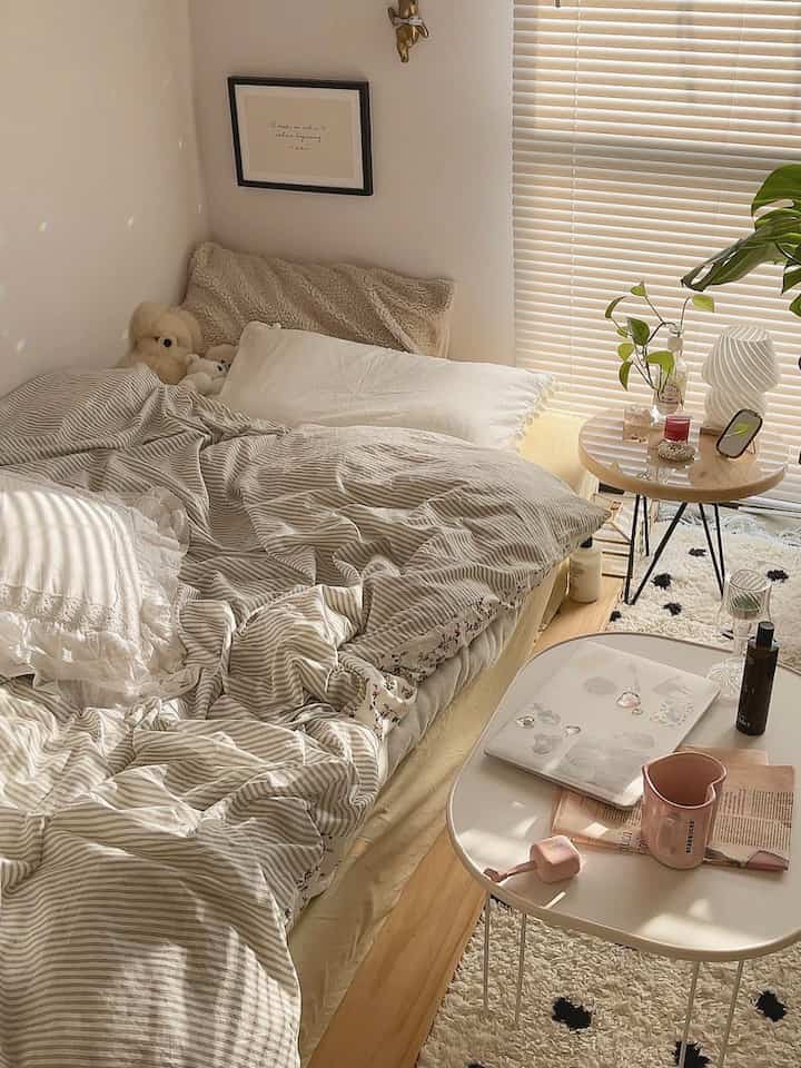 ナチュラルな色調の寝室、ベージュの寝具と丸いナイトテーブル、ホワイトブラインドが配置された雰囲気のある空間