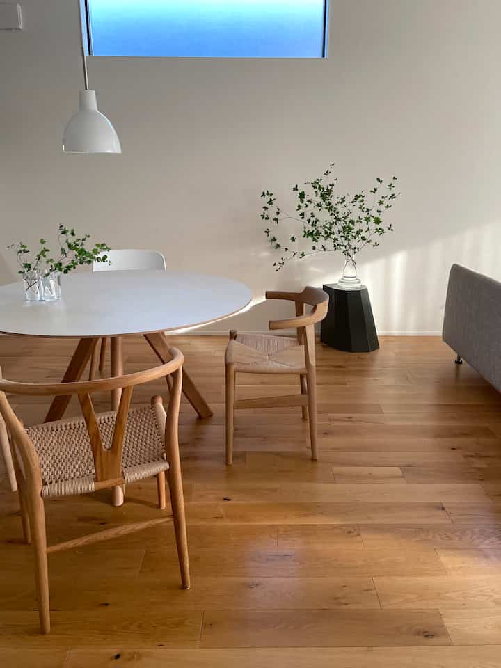 Natural tone living/dining space featuring a round dining table, wooden chairs, and green branch decor with a warm and clean atmosphere