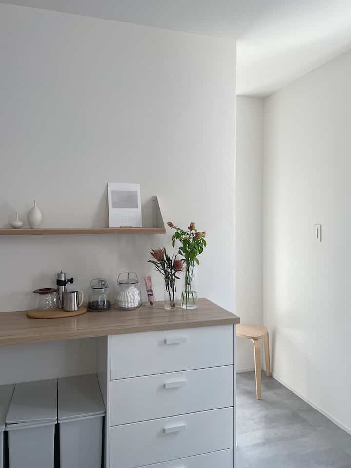 白と木目調が調和したキッチン、スツールと花瓶が配置された印象的な空間