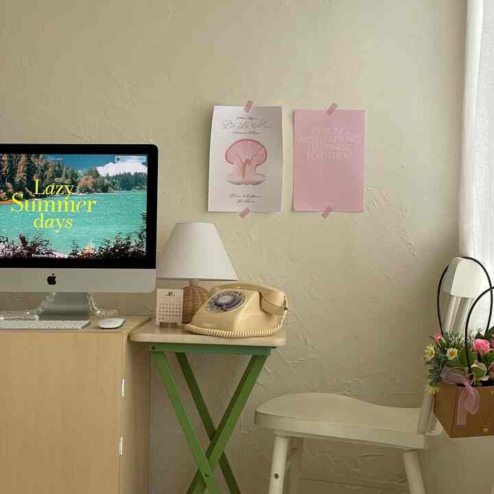 ベージュトーンの壁と自然光が差し込む小さなホームオフィス空間。木製デスクにiMac、ヴィンテージの黄色い電話機と白い椅子が配置された落ち着いた雰囲気のインテリア