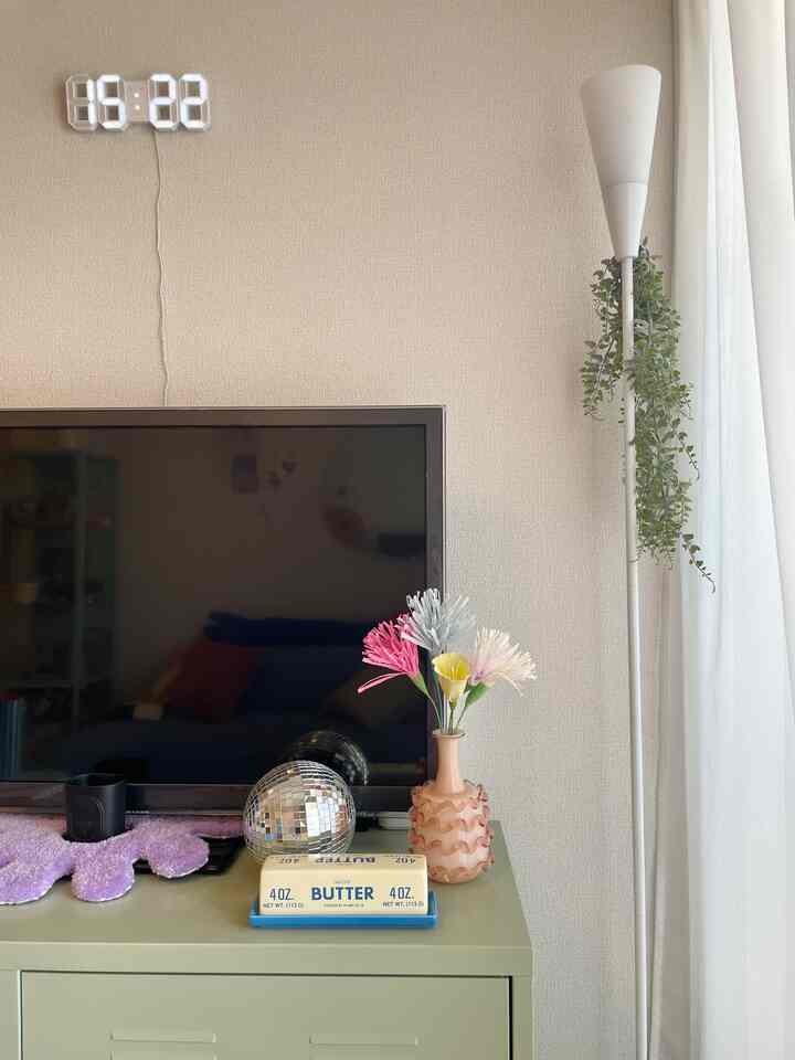 白い壁とミント色のキャビネットが配置されたリビング、テレビと花瓶、フロアランプが調和したシンプルなインテリア