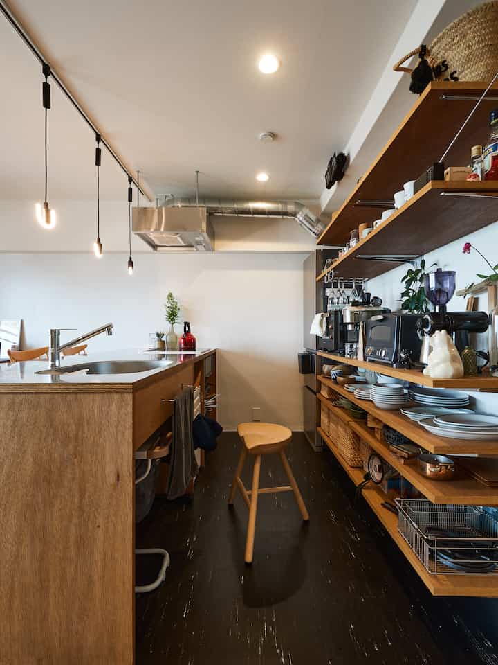 Natural wood tones and black flooring modern kitchen for a single household, featuring a central stool and open shelving creating a practical space