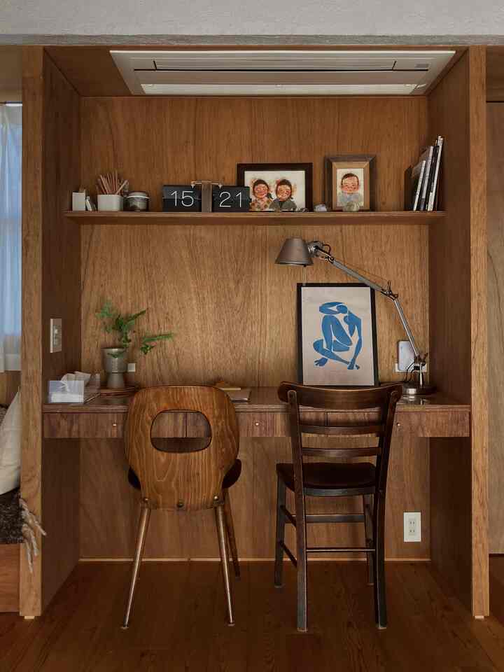 温かみのある木目調のリビングのホームオフィス、造り付けのデスクと椅子、テーブルランプが配置された落ち着いた作業空間