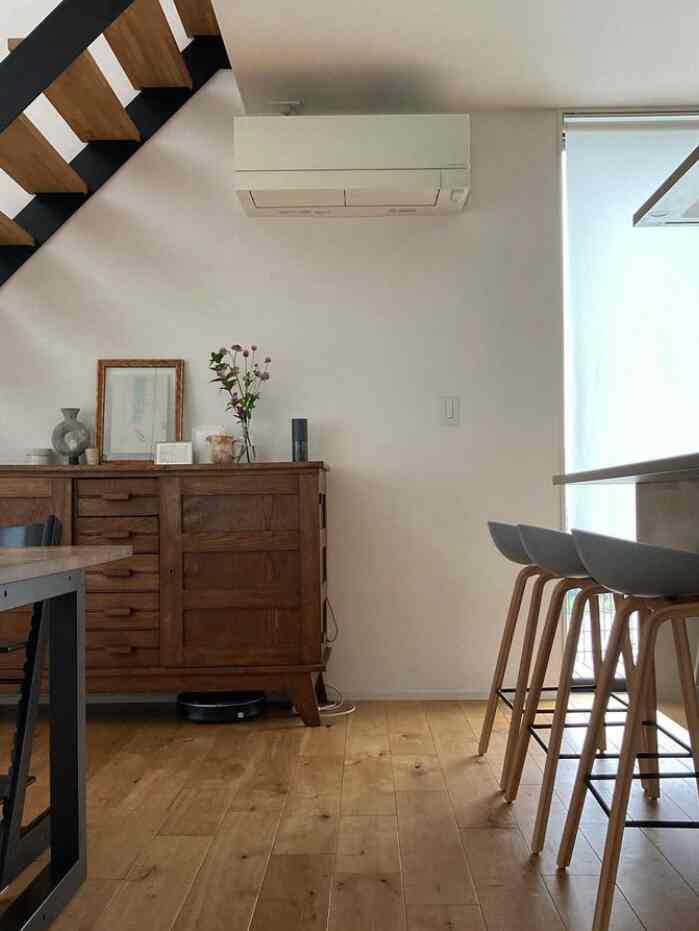 木目調の床と白い壁のキッチンスペース、バースツールと木製の収納キャビネットが配置されたミニマルなインテリア