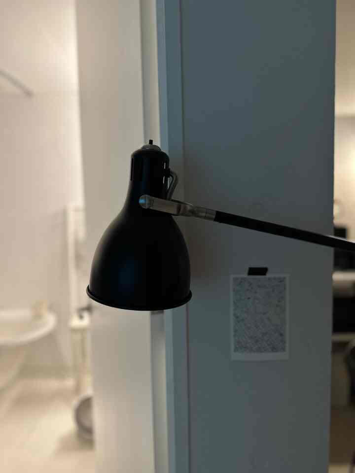 壁に取り付けられた黒いブラケットライト、ぼかされた背景に暗い灰色の室内空間の一部が見える