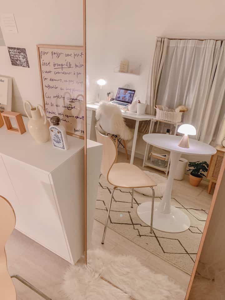 アイボリーとナチュラルカラーの小さいワンルーム、壁に大きなスタンドミラーとシンプルなデザインチェアが配置された落ち着いた雰囲気の空間