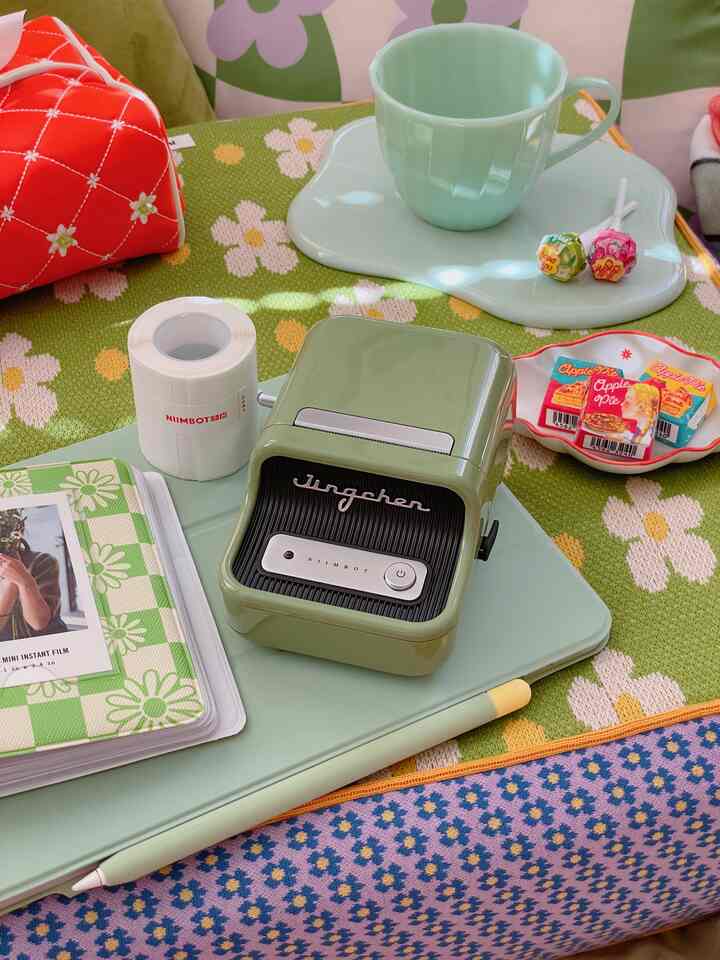 ライトグリーンのテーブル上にレトロなラベルライターと花柄のクッションが配置されたかわいい作業スペース