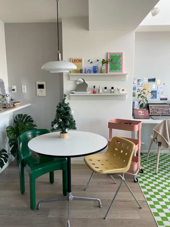 グリーンとピンクの色調のダイニングスペース、白い丸テーブルとモダンなペンダントライト、ピンクのキッチンカートが配置された清潔で落ち着いたインテリア