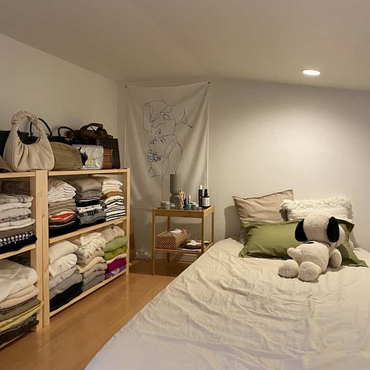 白い壁と木目調床のロフト寝室、整頓された収納棚とシンプルな寝具が配された落ち着いた空間