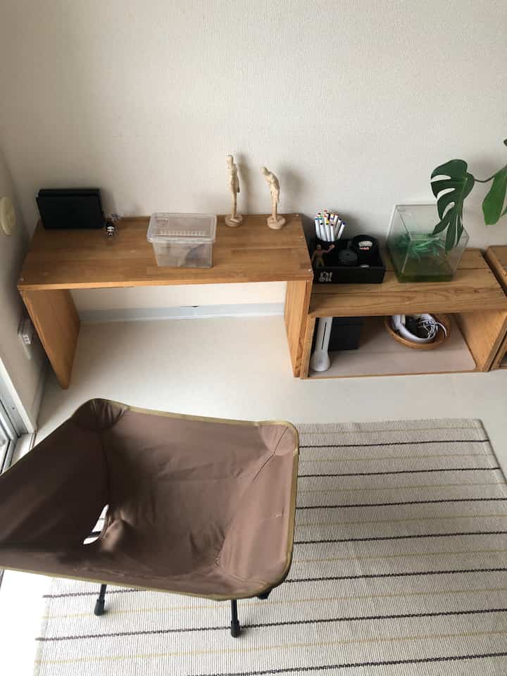 ナチュラルな木目調とベージュのラグが調和する子供部屋、多目的テーブルと植物が配置された雰囲気のある空間