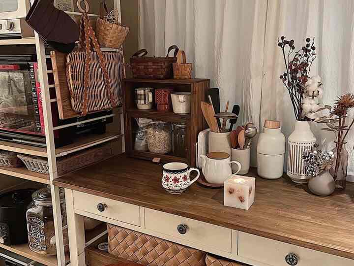 温かみのある木目調とベージュのキャビネットが調和したキッチンカフェスペース、キッチン用品やバスケットが配置されて落ち着いた雰囲気のインテリア