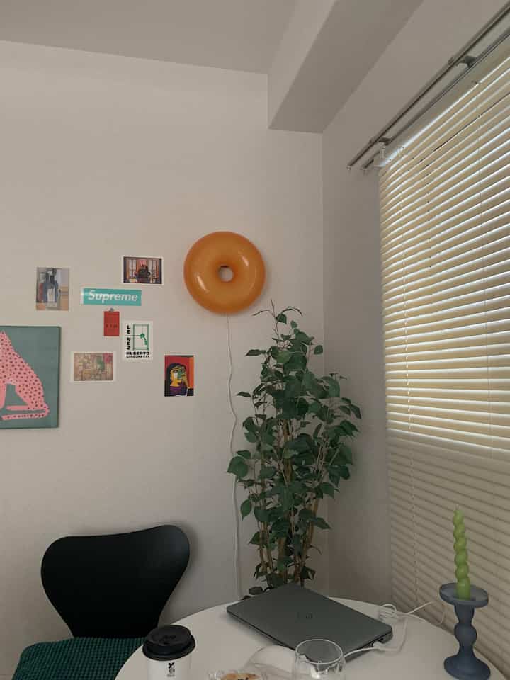 白い壁と丸い白テーブル、ブラインドがある狭めのワンルーム空間に黒い椅子と緑の植物が配されたシンプルなインテリア