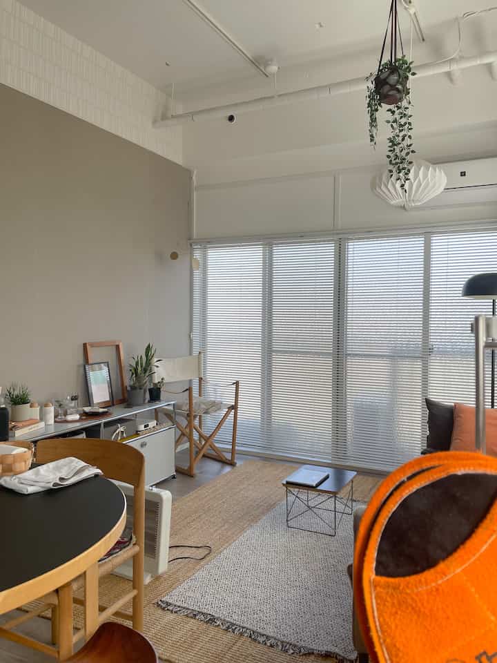 ナチュラルな色調のキッチン兼リビング空間、平織りラグとアームチェア、植物が配置された雰囲気のあるインテリア。