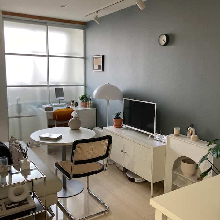 白を基調としたリビング、テレビ台と丸いダイニングテーブル、デスクが配置されたモダンで清潔感のあるインテリア