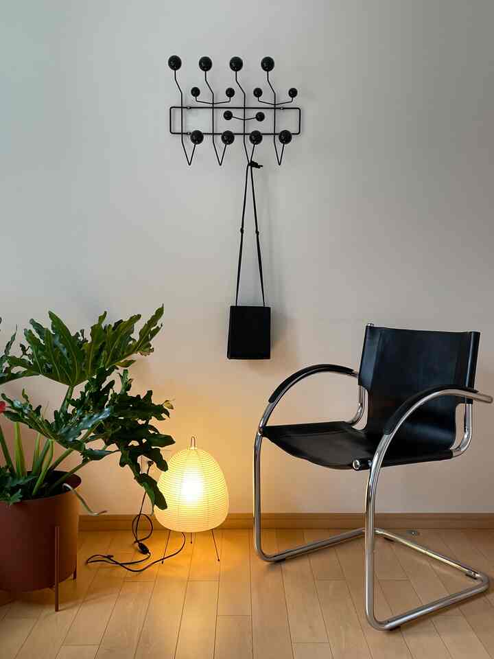 木目調の床と白い壁を背景に、黒いレザーアームチェアと大きな緑の植物、温かみのある光を放つフロアランプが置かれたモダンな玄関空間