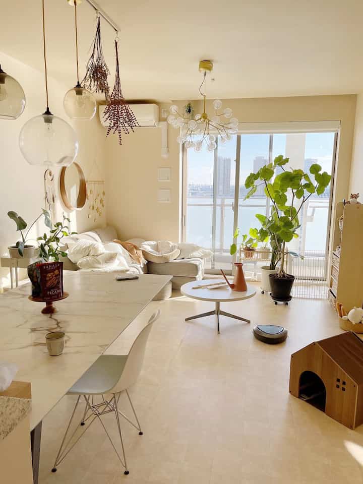 A natural-toned living room featuring white, brown, and green plants, with a pet house for a dog and a comfortable sofa arranged in a relaxed setting.