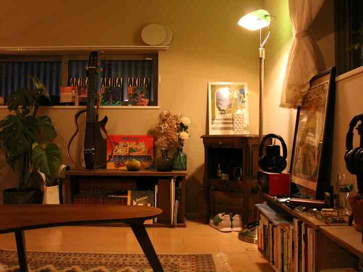 温かみのある木目調とベージュ色調のリビング、DIY本棚とアールデコ風の小さなキャビネットが配置された雰囲気のある空間