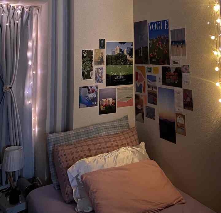 ピンクとアイボリーの寝具がある小さな寝室、壁にポスターとストリングライトが配置された雰囲気のある空間