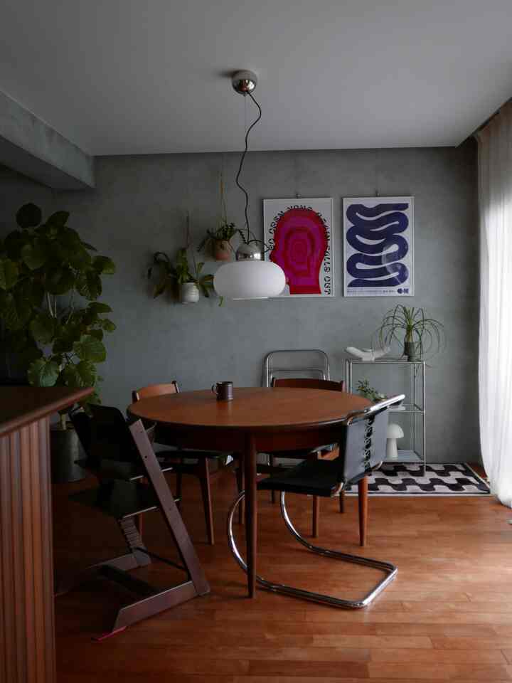 Natural-toned living and dining room with a round wooden dining table and chairs, pendant light, wall posters, and plants creating a cozy atmosphere