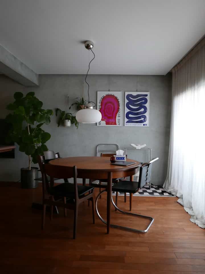 ナチュラルな木目調のダイニング、木製テーブルとチェア、ペンダントライトとポスターが配置された落ち着いた空間