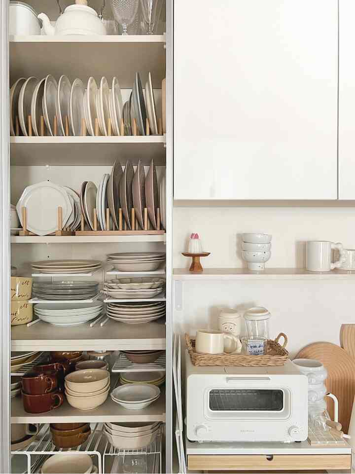 White and natural toned kitchen featuring neatly organized plate storage and small appliances creating a cozy atmosphere