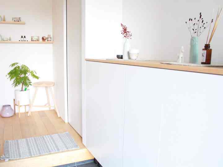 白と木目調の玄関、植物を置いたシューズラックがあるシンプルな空間
