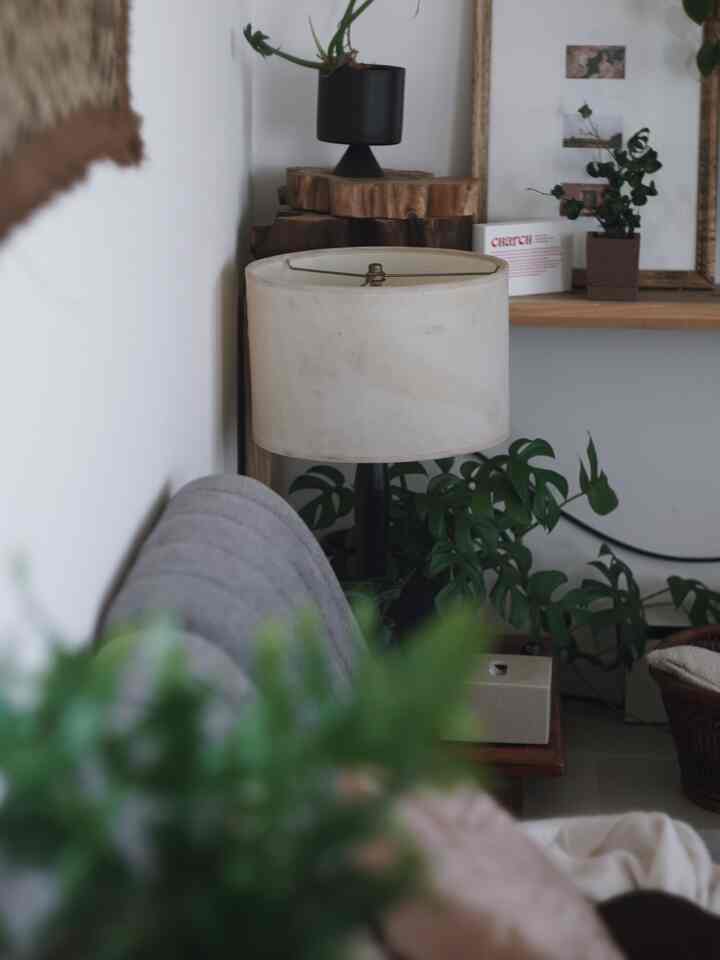 ナチュラルカラーのリビング、グレーのコーナーソファとフロアランプ、緑豊かな植物が調和した雰囲気のあるインテリア