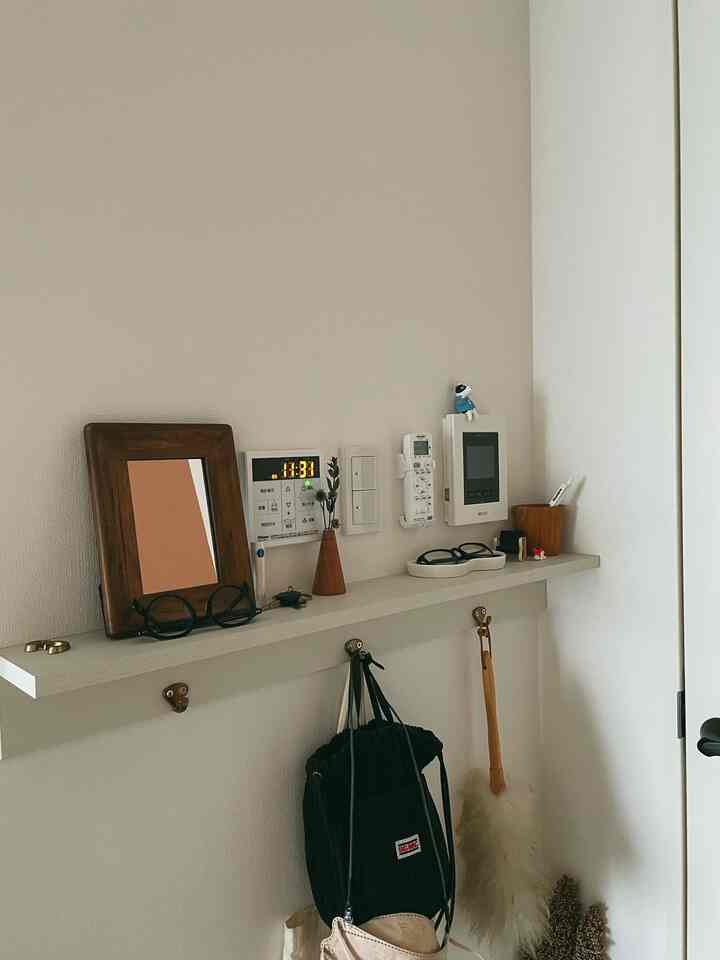 ホワイトトーンの玄関空間に壁付け棚とフック、メガネトレーが配置された実用的でミニマルな収納インテリア