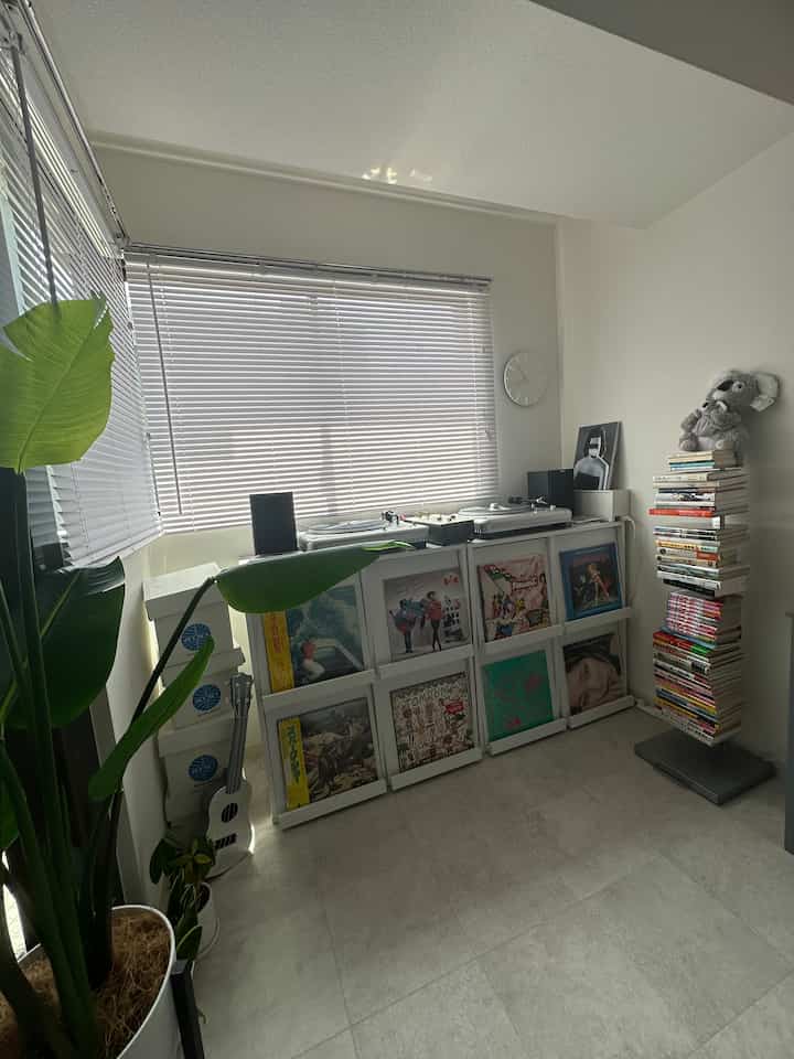 Bright white-toned living room with blinds on windows and record players arranged for a cozy music listening space