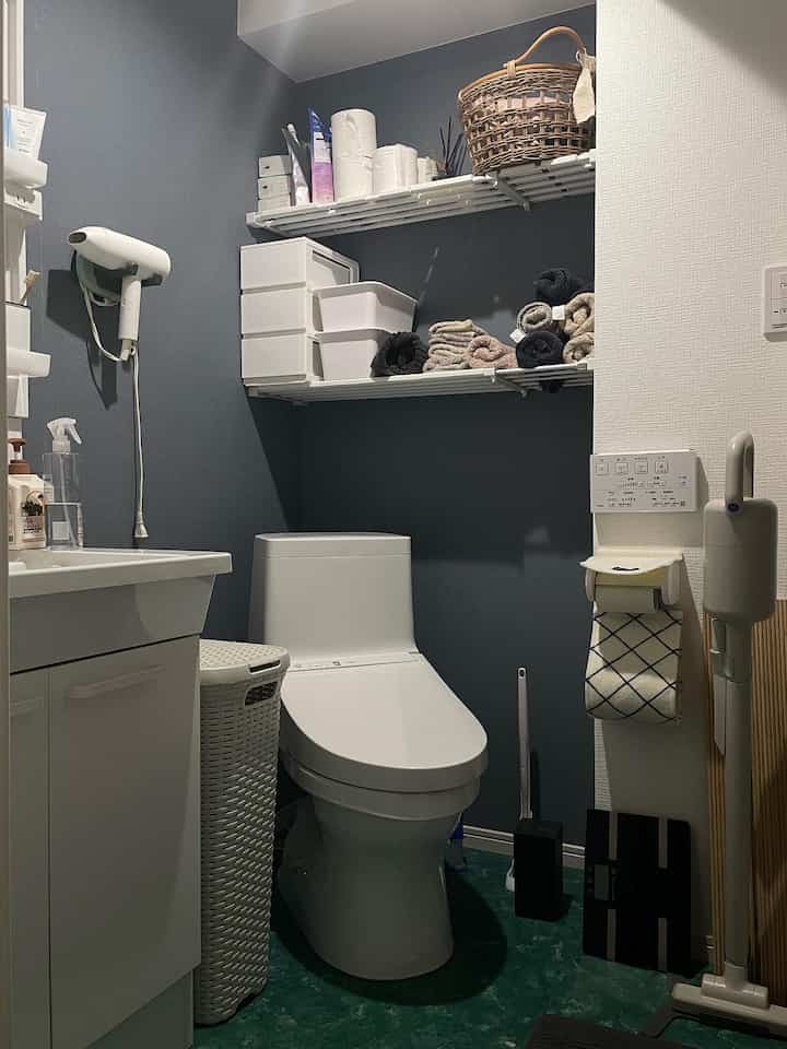 ネイビーカラーの壁と白の設備が調和するコンパクトなバスルーム、整然としたタオルと収納棚が配置された清潔感のある空間