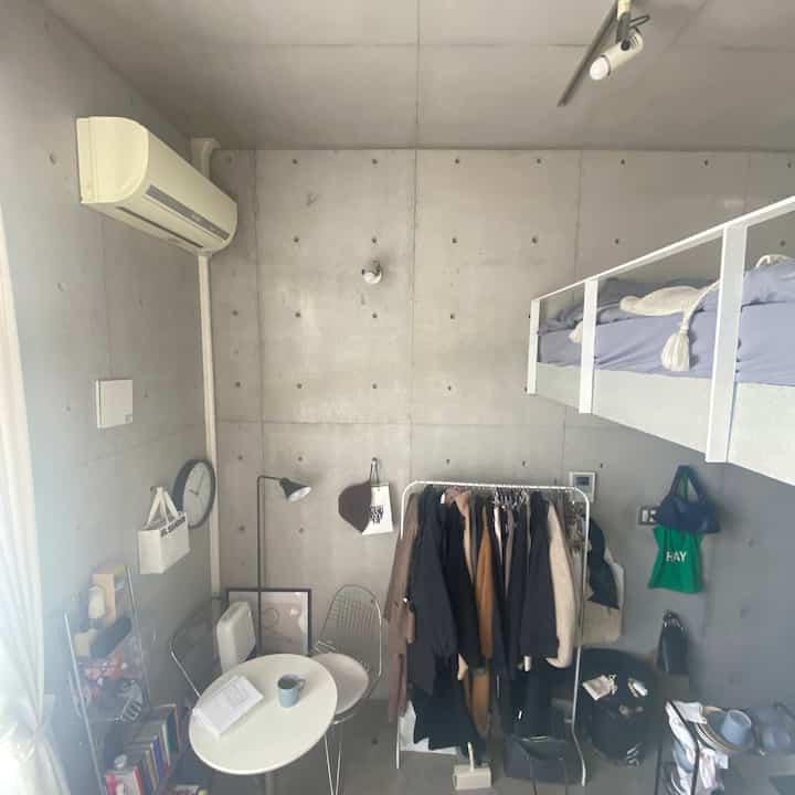 White and gray toned loft room featuring a bed and clothing rack in a simple, compact space