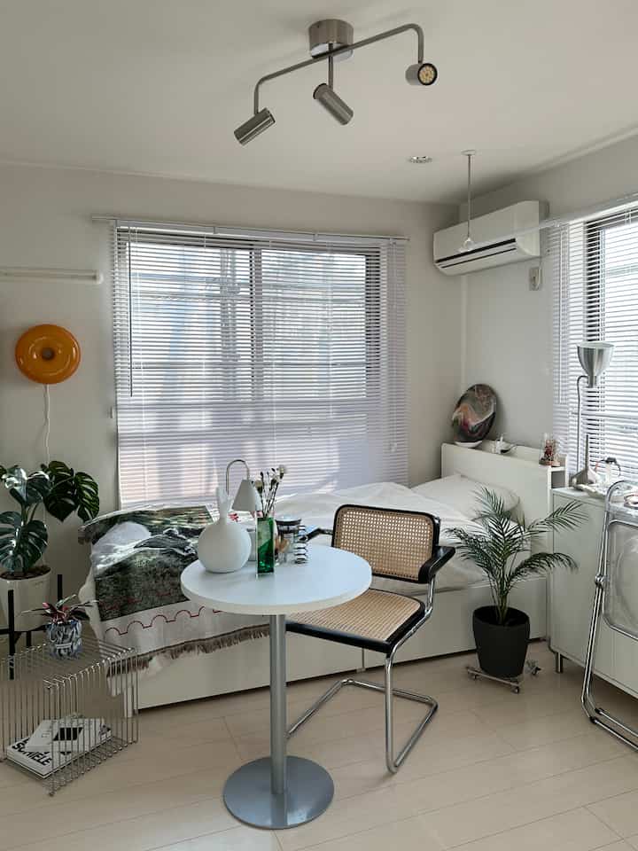 白と木目調の調和が美しい明るいモダンな寝室、丸テーブルとラタンチェア、植物が配された雰囲気のあるインテリア