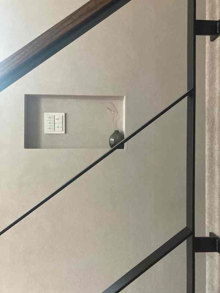 Beige-toned wall with a small niche featuring remote control and switches, decorated simply with a dark vase in minimal interior